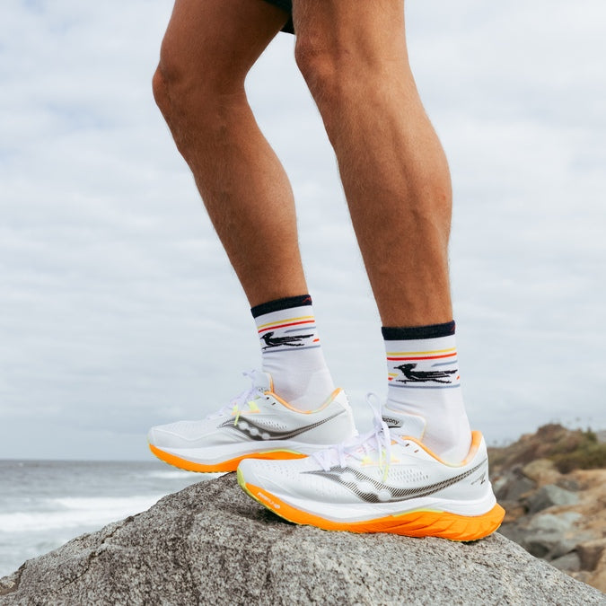 Runner standing on a rock on the shore in Darn Tough Pacer Run Socks