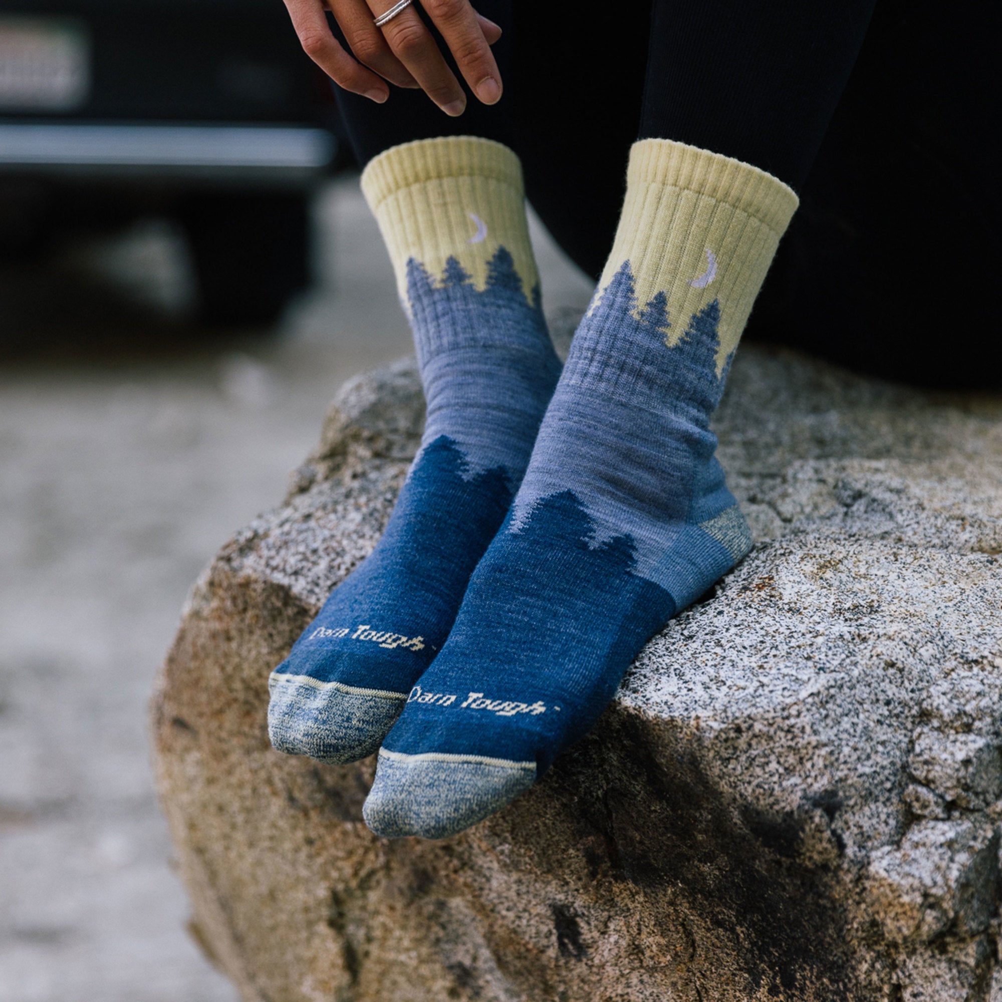 Close up of model sitting on a rock outside wearing women's treeline micro crew hiking sock in ligh denim
