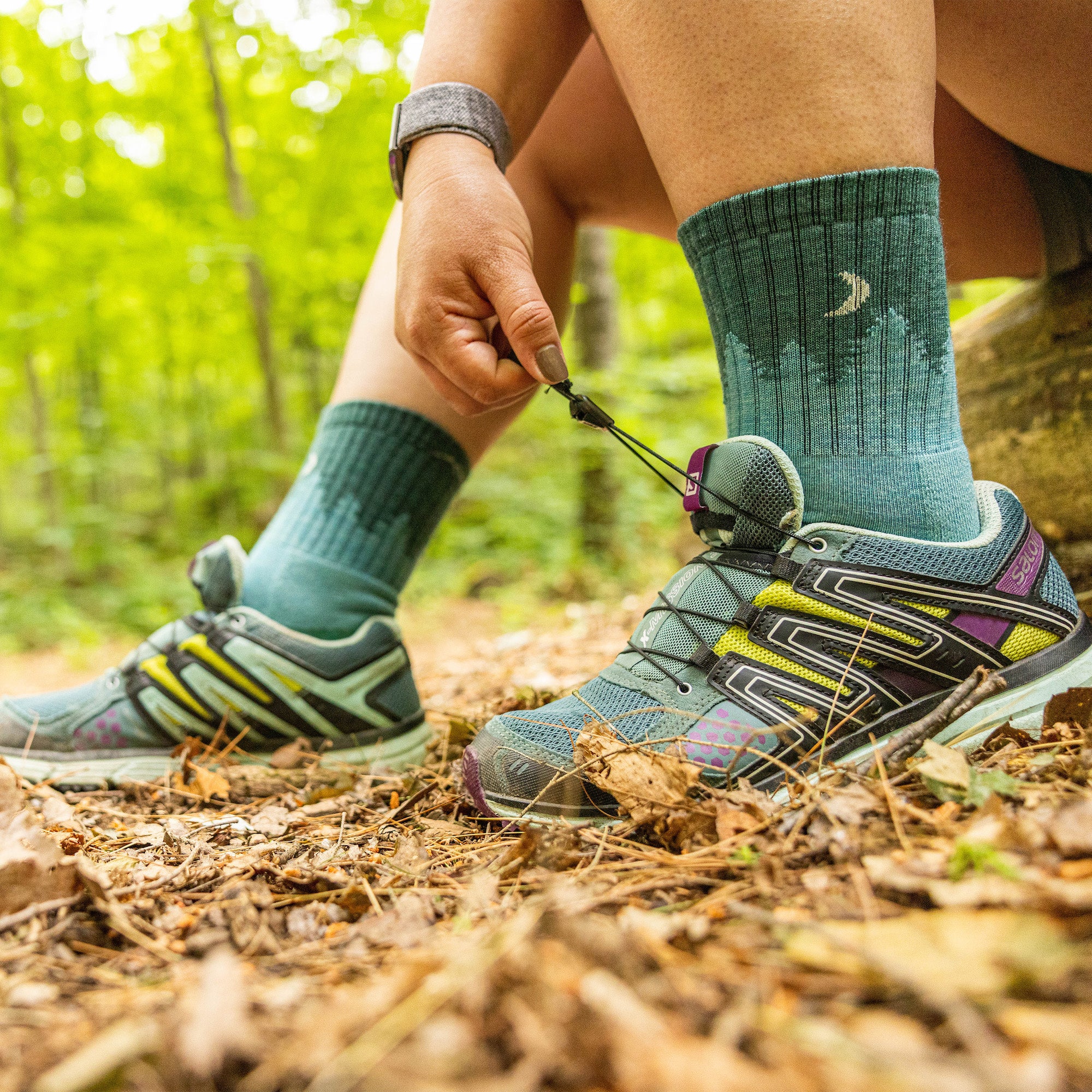 Close up of model sitting on a log outside wearing women's treeline micro crew hiking sock in aqua