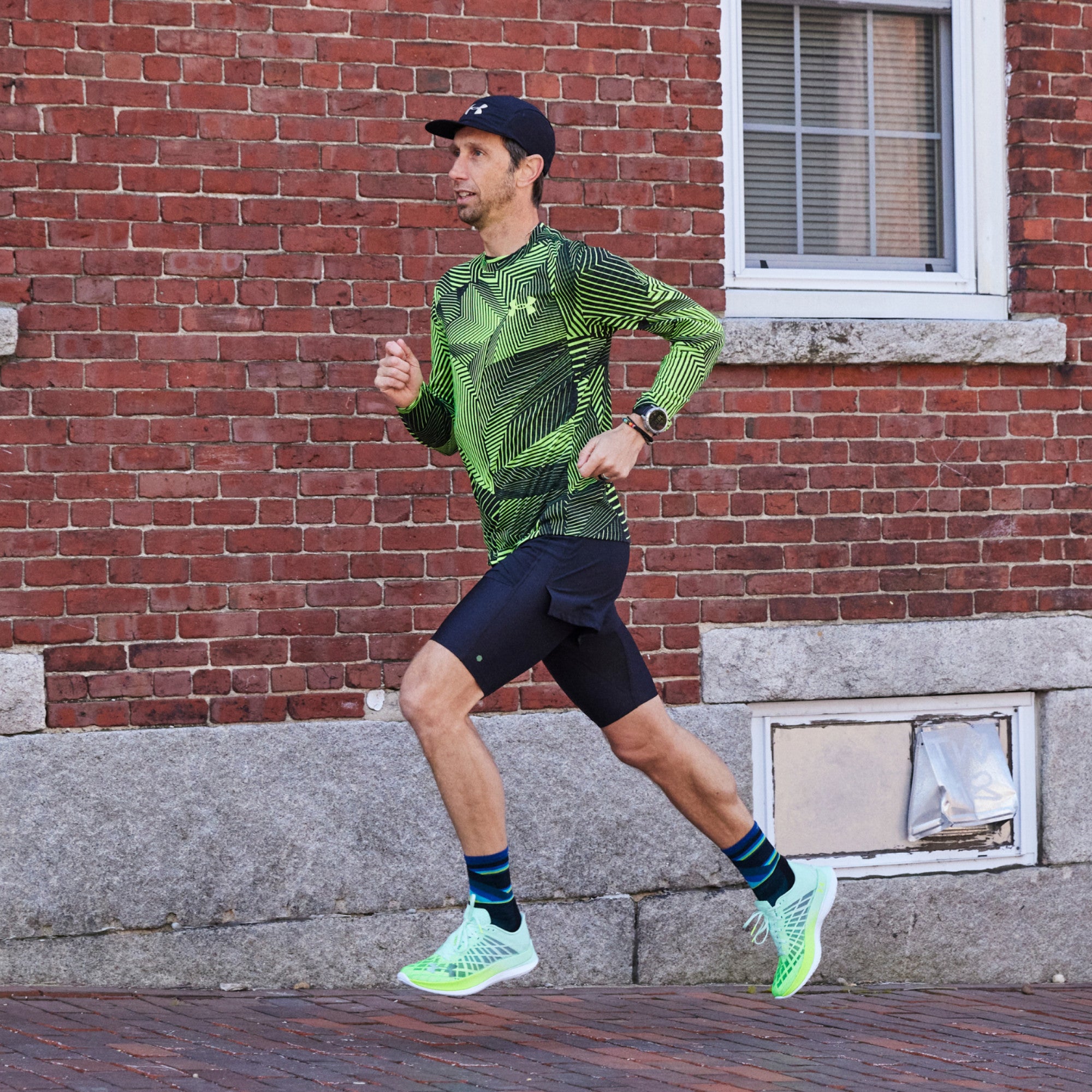 Action shot of model running against brick background while wearing 1056 socks in black colorway