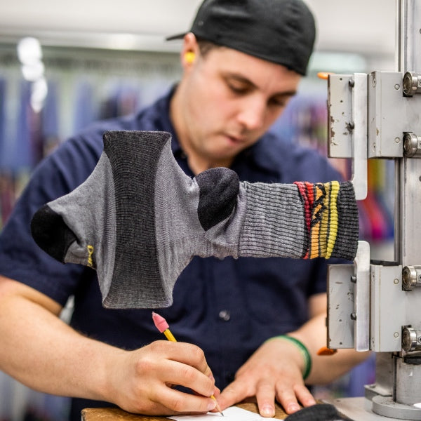 Visit the Guarantee for Life page. Image of Darn Tough employee testing the quality of a sock
