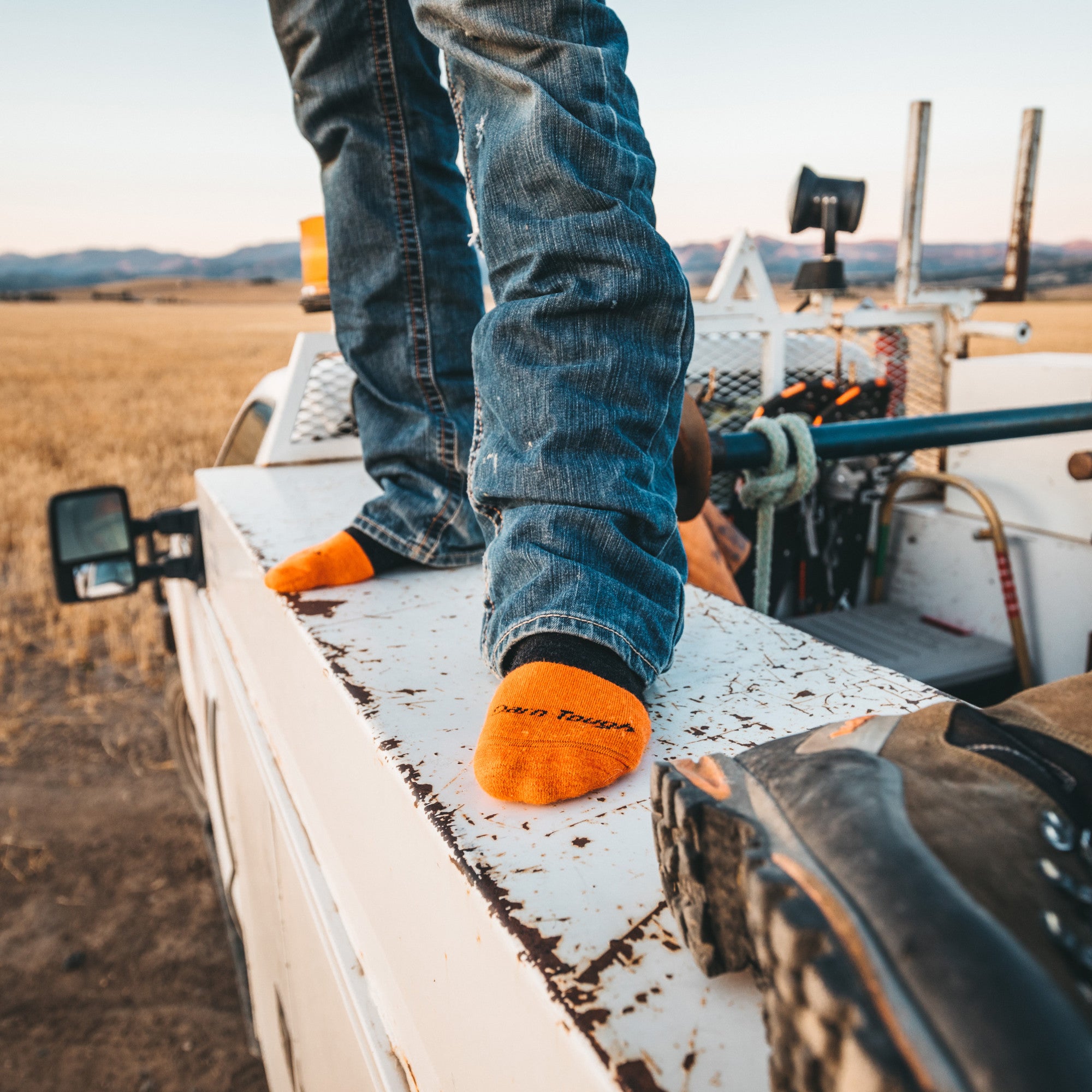 Close up shot of model standing on the side of a truck bed wearing the men's steely boot work sock in graphite