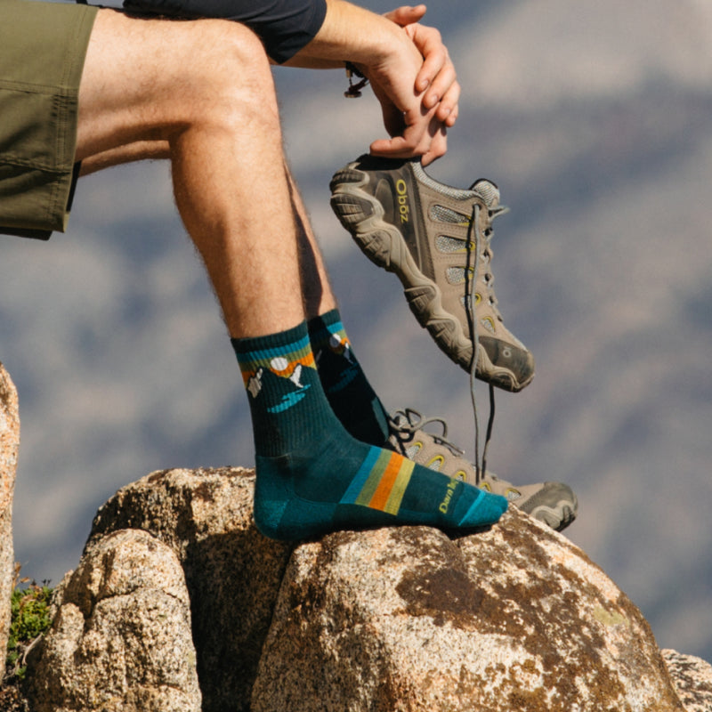A hiker crossing a stream wearing new darn tough hiking socks with stripes