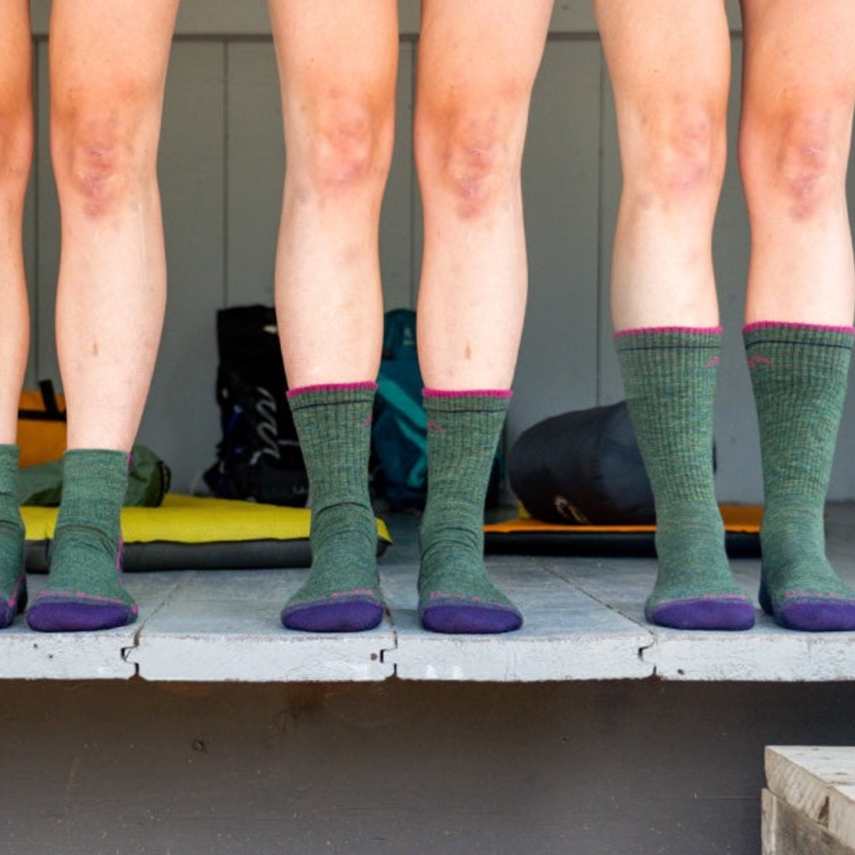 Four people standing next to each other in various heights of green Darn Tough Socks