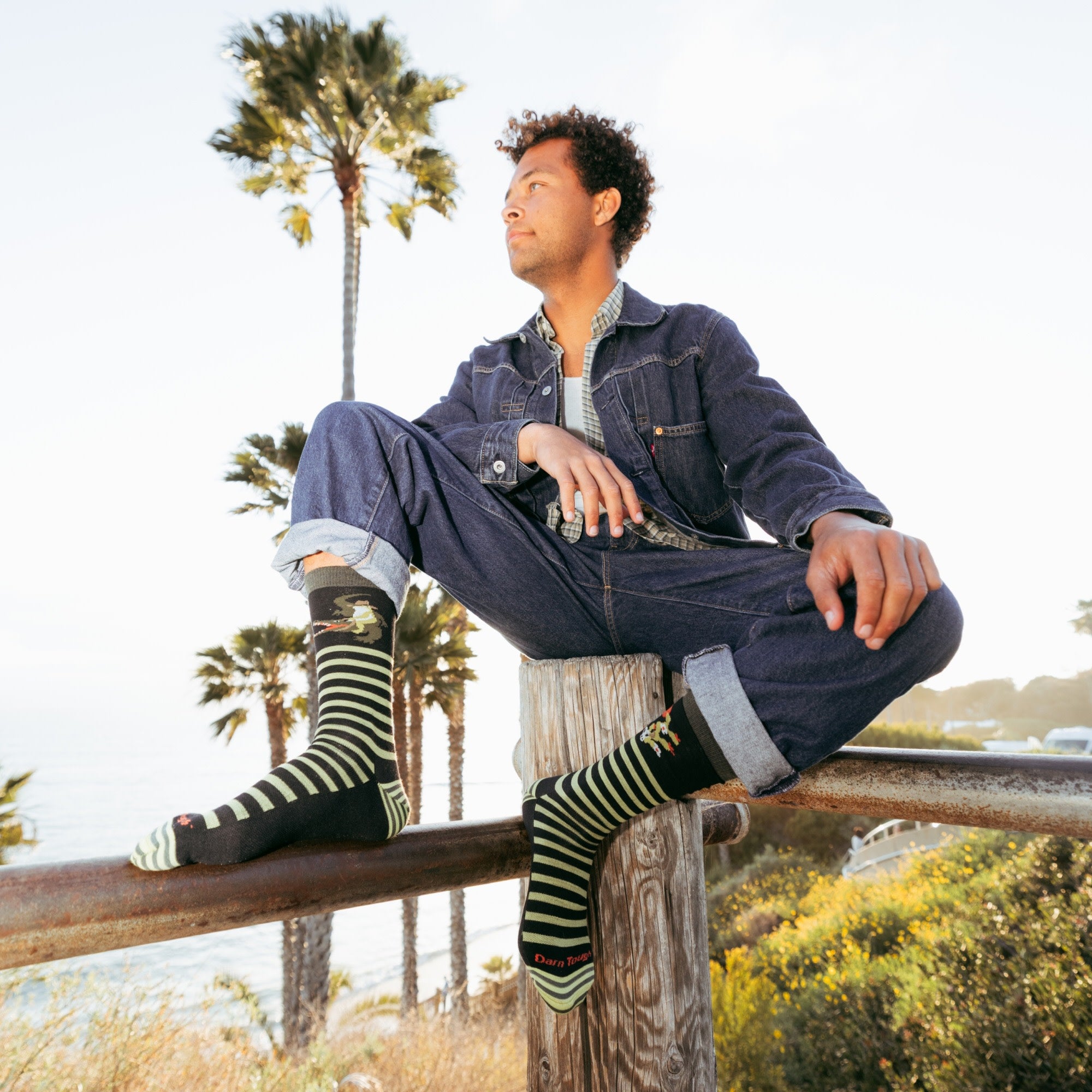 model sitting on a fence poll wearing the 6066 animal haus lightweight lifestyle crew sock in gator green