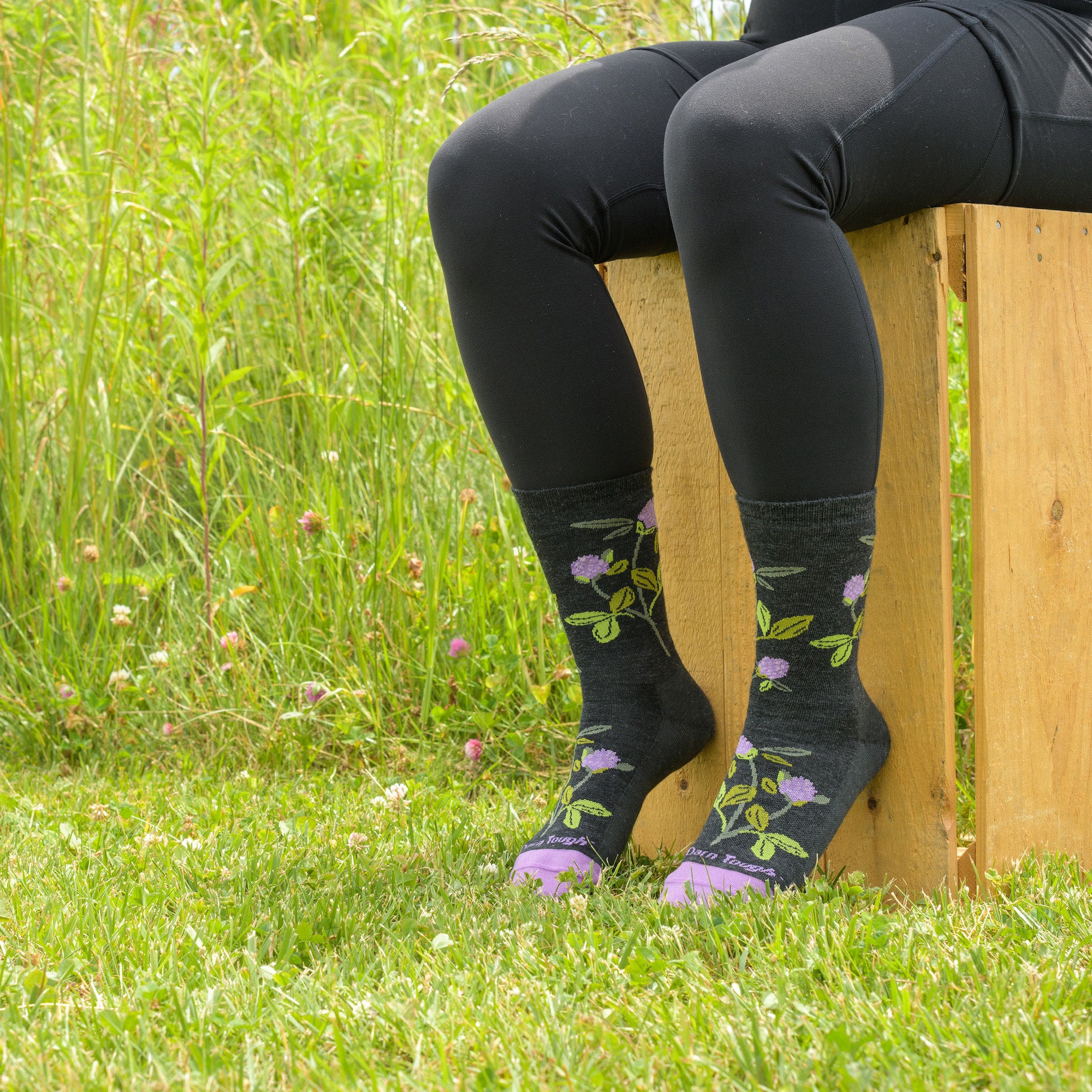 Close up of model sitting on a wooden box in the grass wearing the women's blossom crew lifestyle socks in charcoal