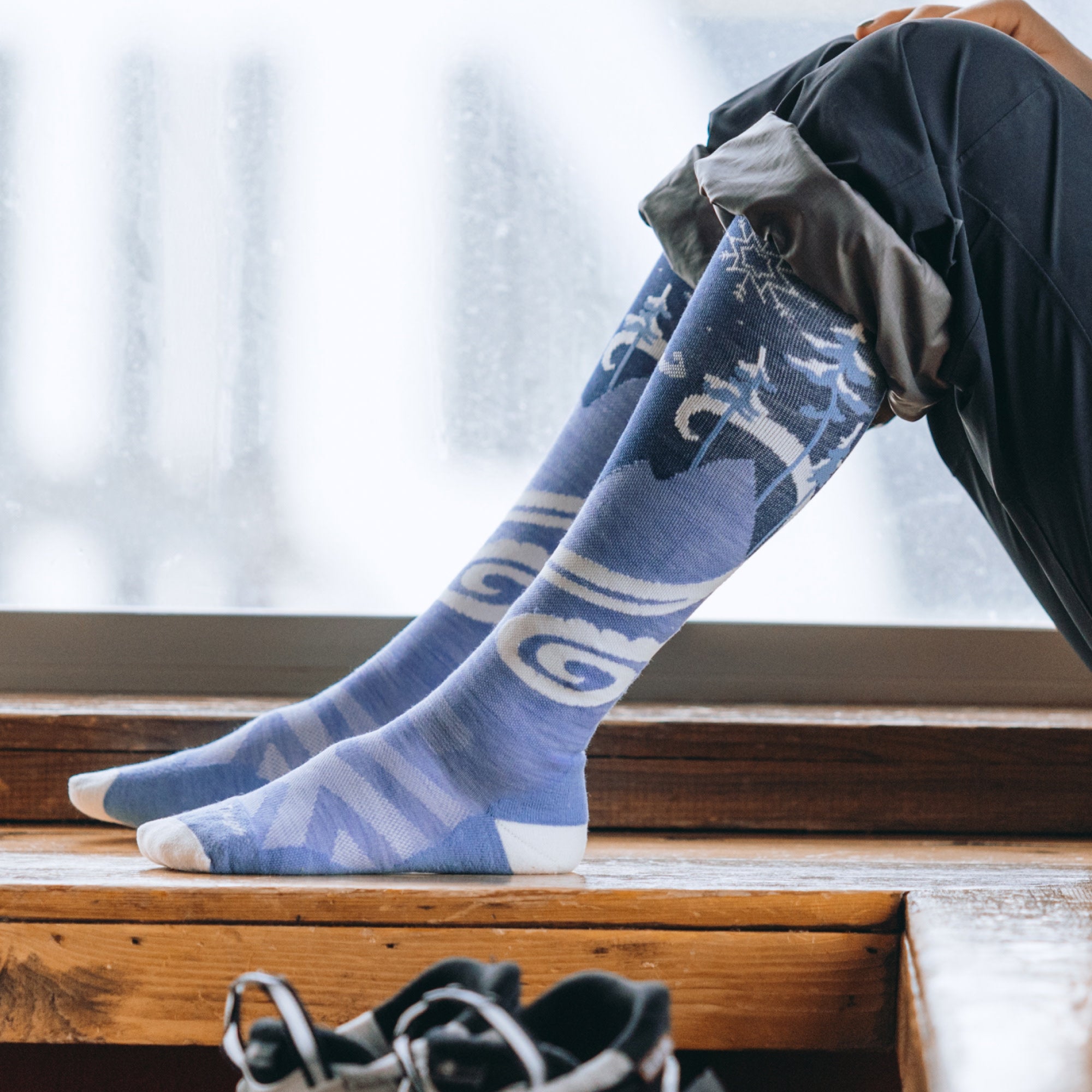 models feet on a wood bench wearing the 8054 swirlwind over the calf sock in midnight 