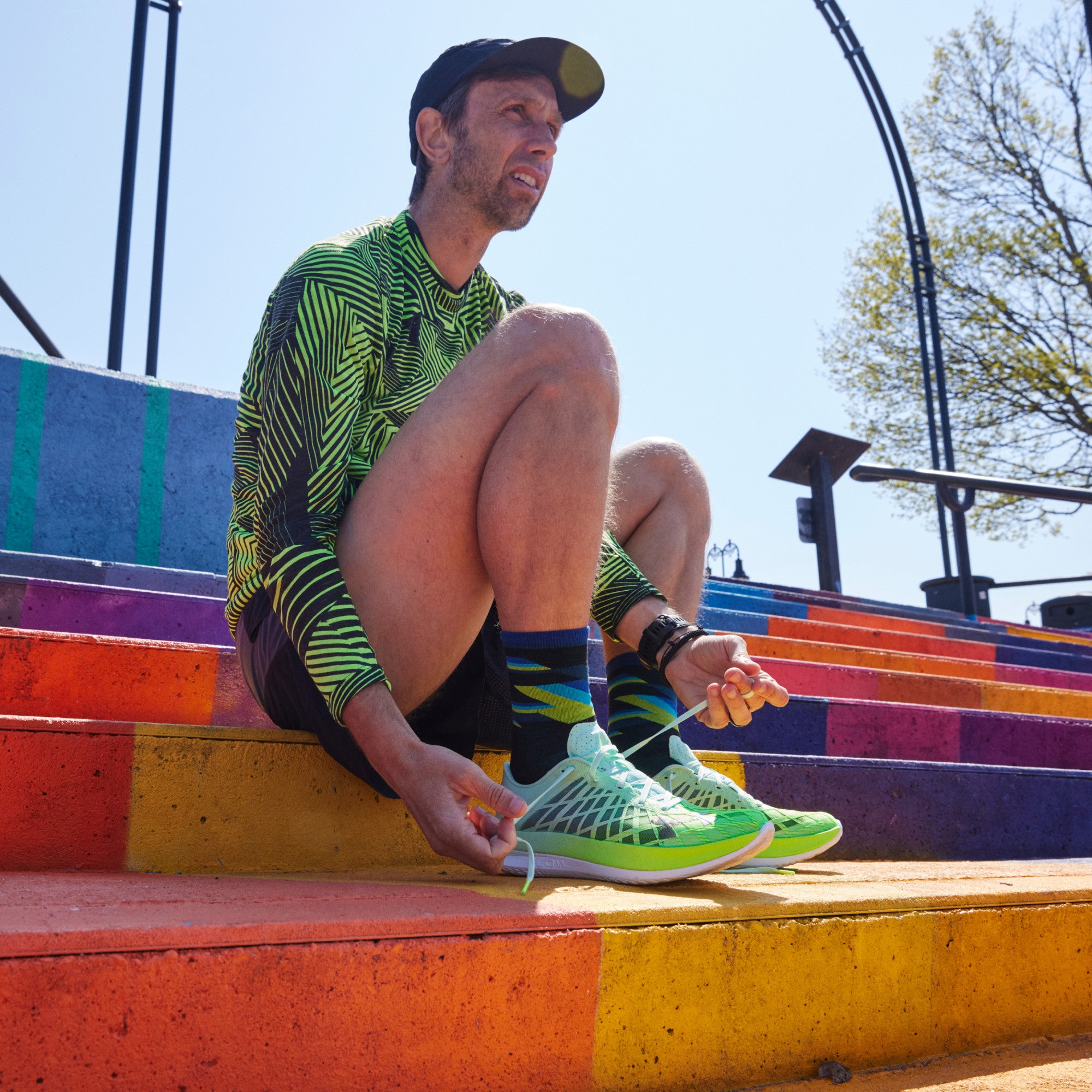 Model sitting on colorfully painted concrete steps while wearing 1056 socks in black colorway and lacing up bright green running shoes.