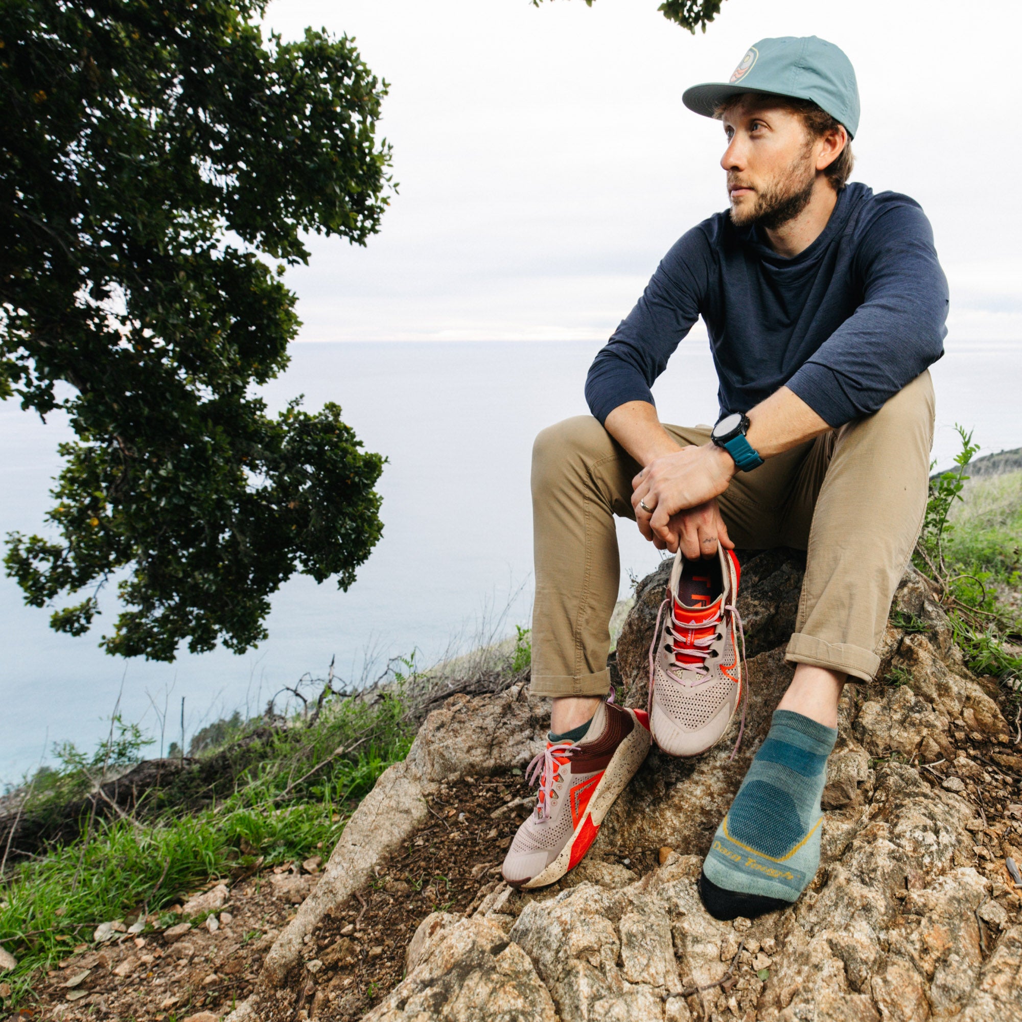 Model sitting on rock hold sneaker wearing the 1990 Light Hiker No show hiking sock in seafoam