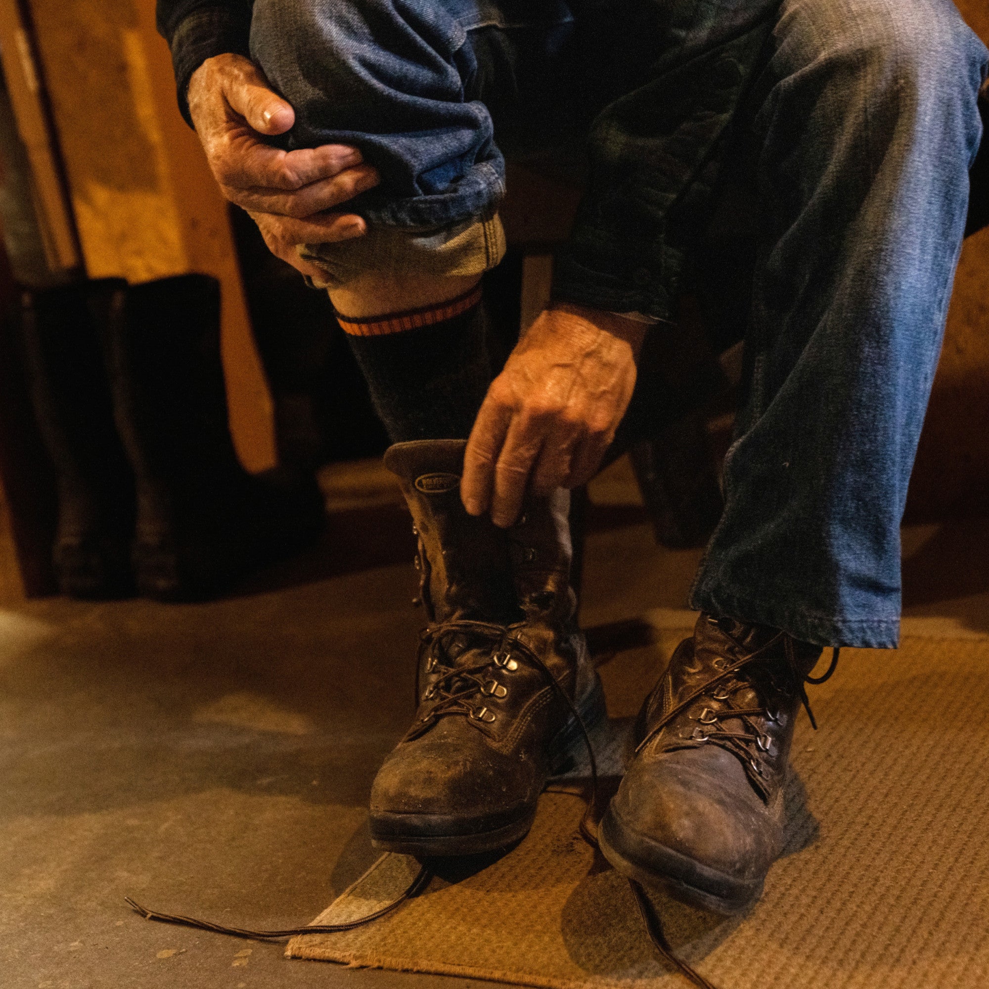 Close up shot of model in blue jeans and 2006 socks in graphite pulling on brwon work boots