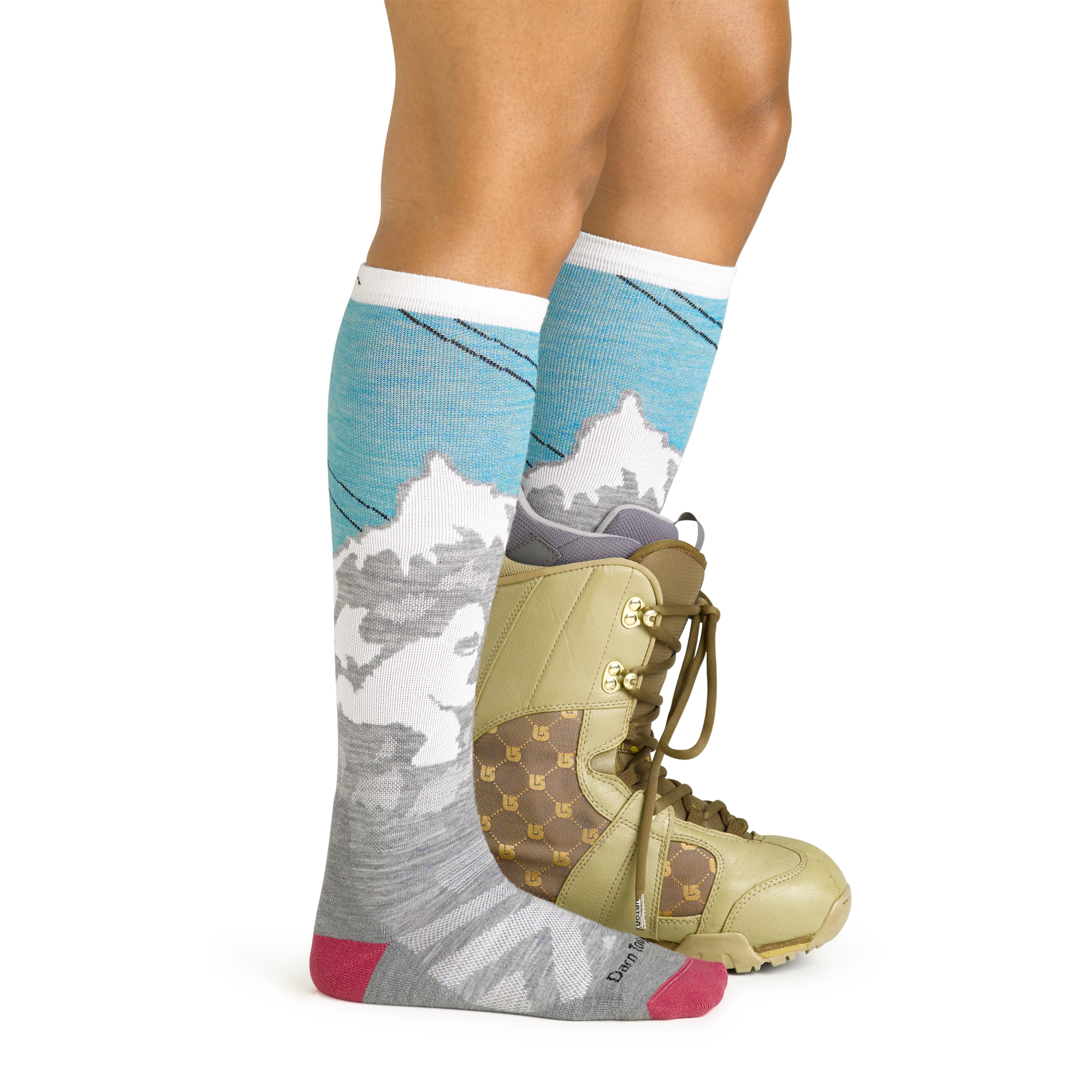 Side studio shot of model wearing women's yeti over-the-calf snow sock in aqua with green snowboard boot on left foot