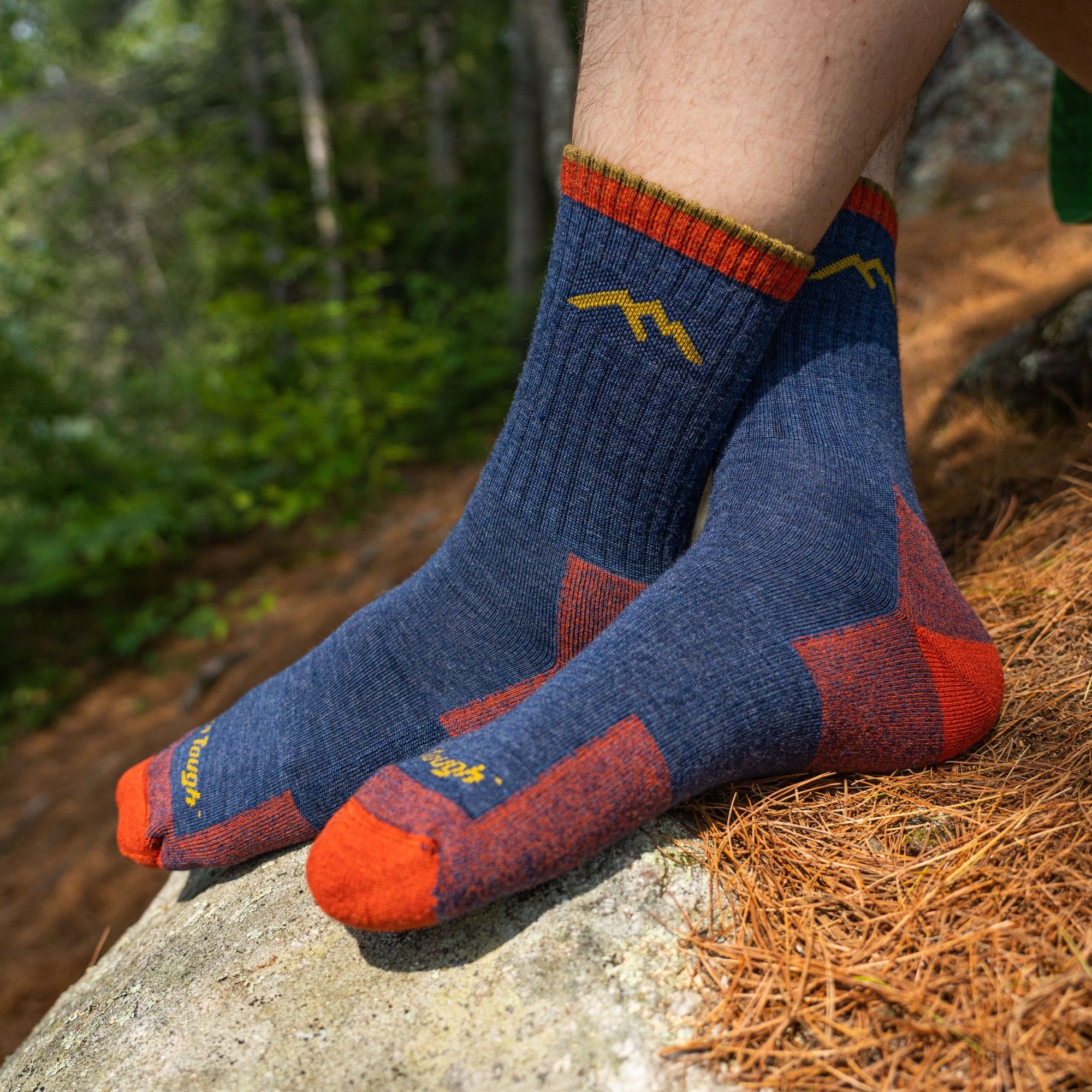Model sitting on a hiking trail with no shoes wearing the men's micro crew hiking sock in denim blue