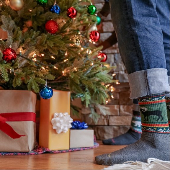 Feet standing by a Christmas tree wearing Darn Tough socks