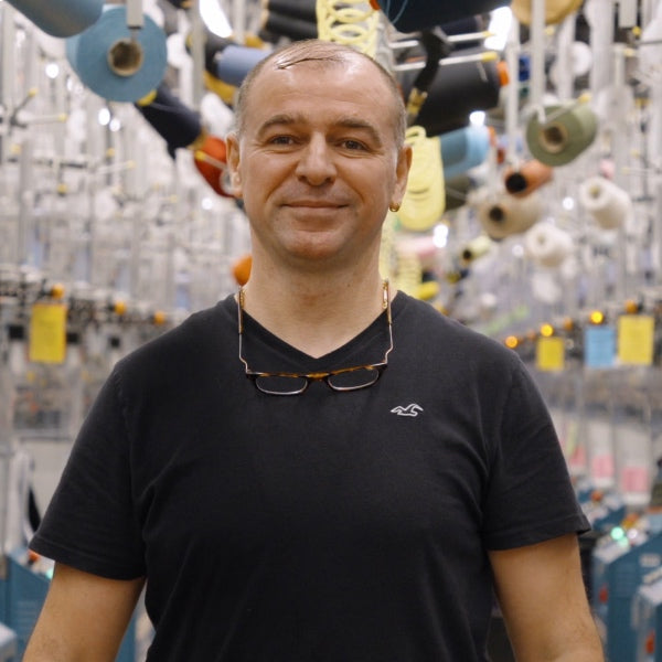 Master Technician Adnan standing in front of knitting machines at the Mill