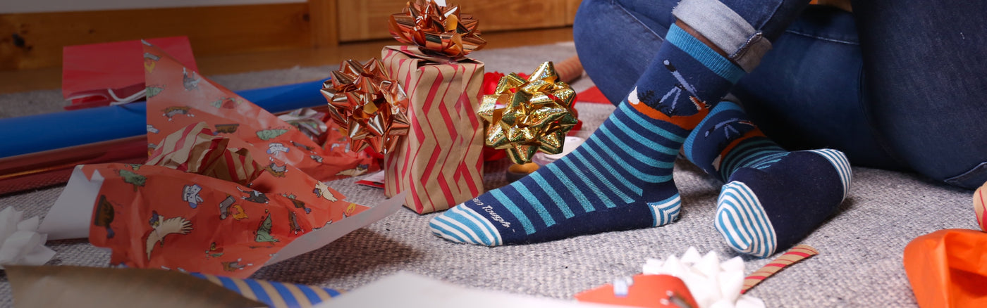 Feet wearing Darn Tough socks next to piles of bows and wrapping paper