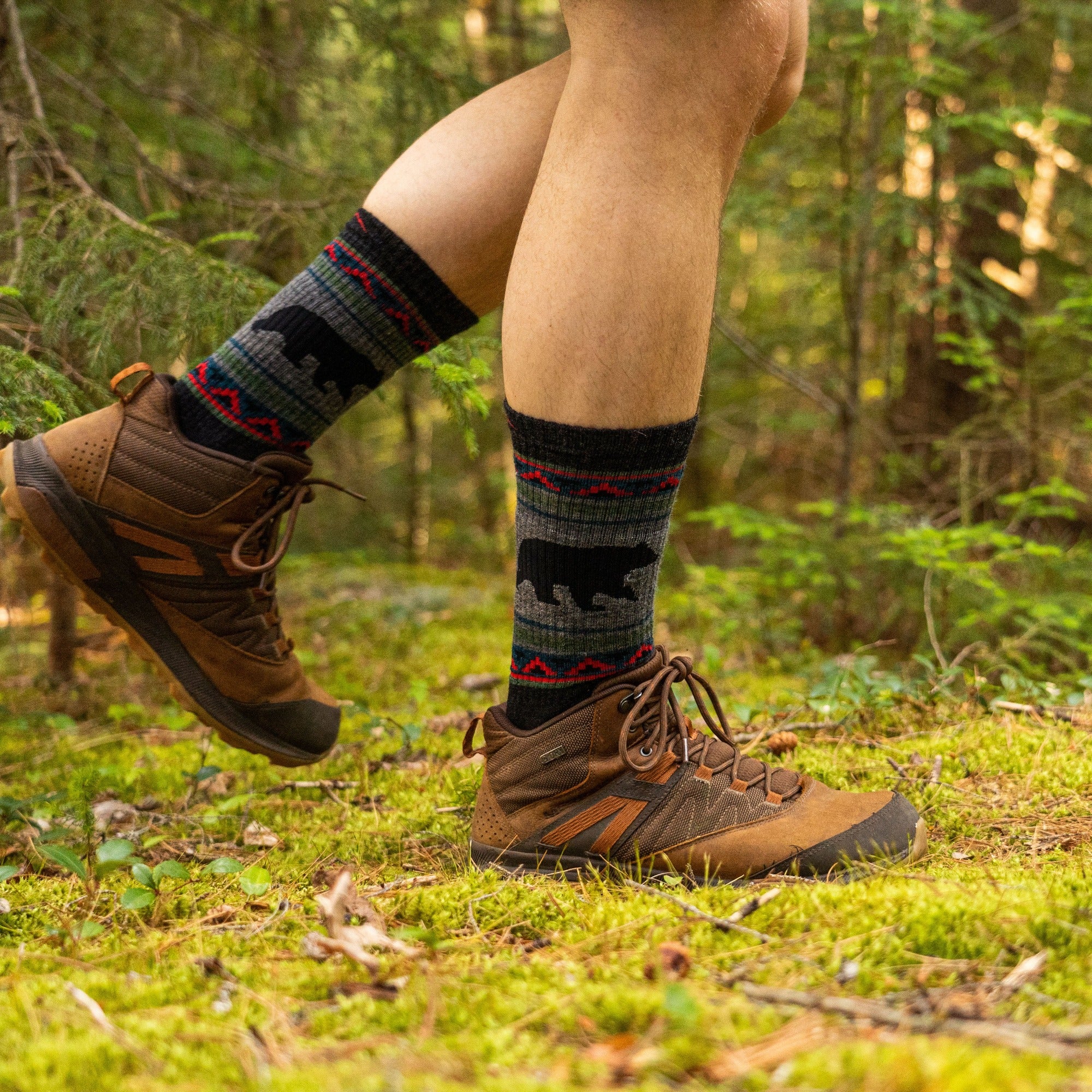 Close up lifestyle image of a man walking on a mossy trail in a forest, wearing hiking boots and VanGrizzle Boot Midweight Hiking Sock in Charcoal