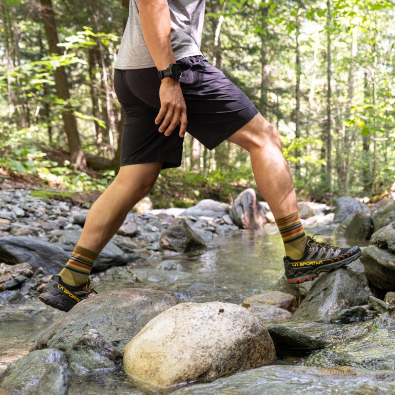 A hiker crossing a stream wearing new darn tough hiking socks with stripes