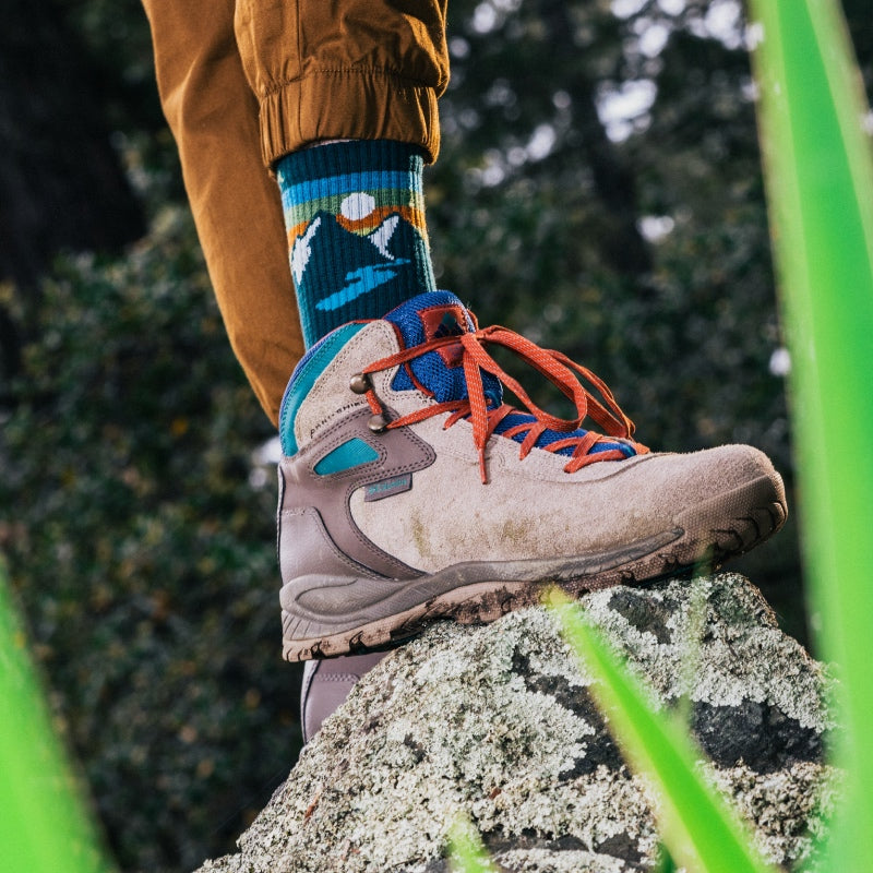 A foot on a rock wearing hiking boots and beautiful Darn Tough hiking socks with a mountain design