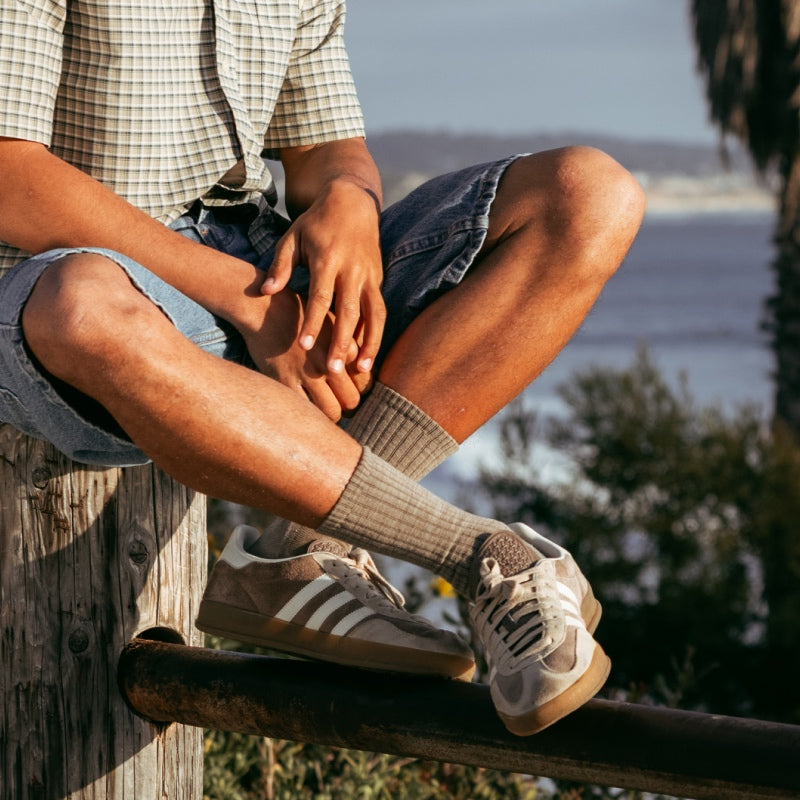 A person seated on a fence post wearing solid tan socks and sneakers