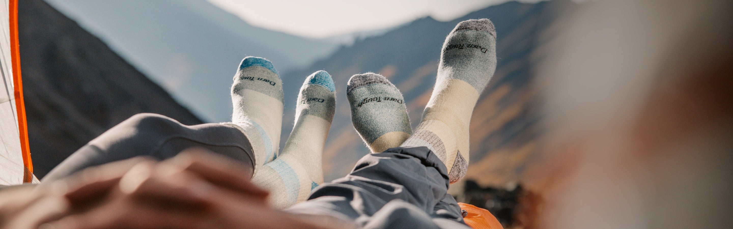 Two pairs of feet in warm merino socks, up on a mountain camping in a tent